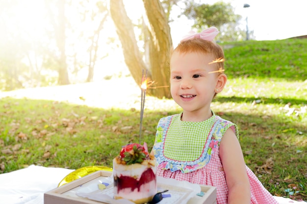 Kostbaar meisje dat naar een kaars kijkt tijdens een picknick op de dag van haar tweede verjaardag
