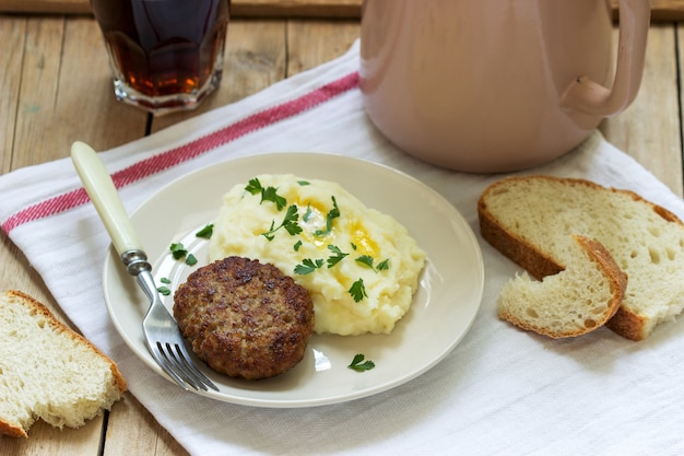 Kotelet, aardappelpuree met boter en peterselie en thee op een houten tafel.