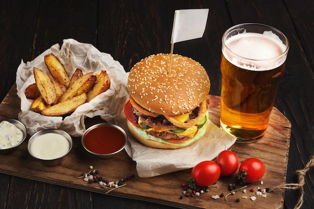 Koud bier en runderhamburger, set sauzen en wedges op houten plank