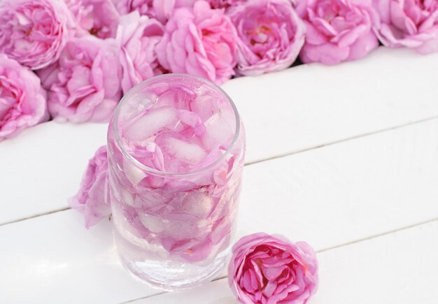 koud drankje gemaakt van lichtroze thee rozenblaadjes in een glas op witte houten planken met roze bloemen