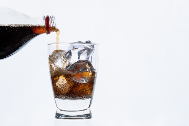 Koud drinken, gieten frisdrank uit fles, glas cola met ijs voor warme en zomer drankje geïsoleerd op een witte muur