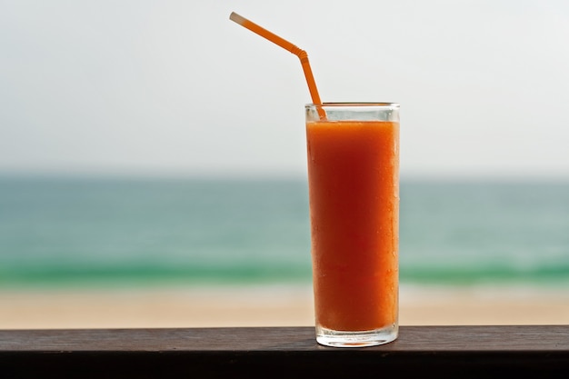 Foto koud het sapglas van het papajafruit met buisje op het oceaanstrand.