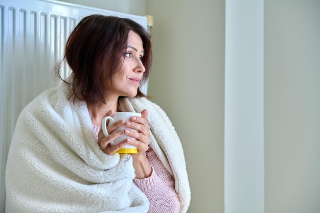 Koud winterherfstseizoen thuis bevroren vrouw in de buurt van verwarmingsradiator