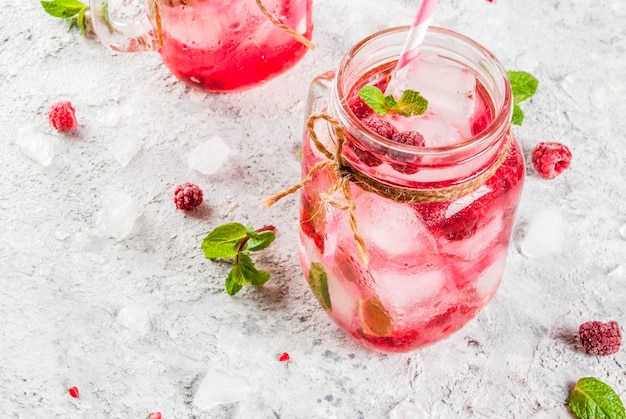 Koud zomers drankje, frambozensangria, limonade of mojito met verse frambozen en siroop, muntblaadjes, op grijze steen copyspace