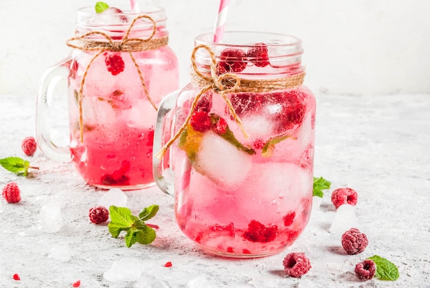 Koud zomers drankje, frambozensangria, limonade of mojito met verse frambozen en siroop, muntblaadjes, op grijze steen copyspace