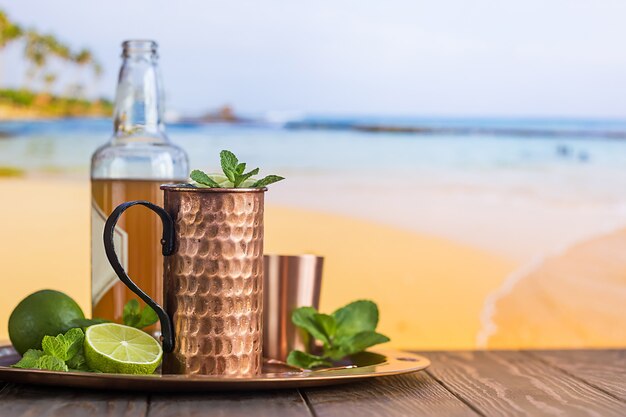 Koude cocktail van Moskou-muilezels met gemberbier, wodka en limoen op het strand en aan zee