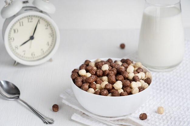 Koude granen in kom geserveerd met lepel en glas melk bereid voor het ontbijt op tafel