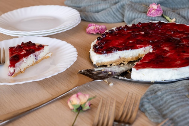 Foto koude kaaskoek met kersen jelly geserveerd op houten tafel met vorken bloemen rozen en groene sluier