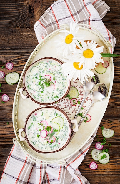 Koude soep met verse komkommers, radijs met yoghurt in kom op houten tafel. Traditioneel Russisch eten - okroshka. Vegetarische maaltijd. Bovenaanzicht Plat leggen