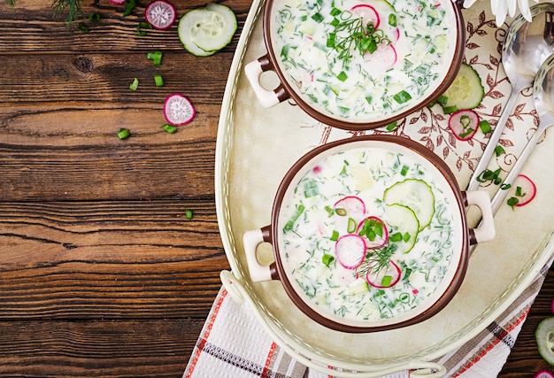 Koude soep met verse komkommers, radijs met yoghurt in kom op houten tafel