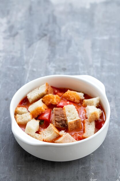 Koude tomatensoep gaspacho met brood in witte kom op keramiek