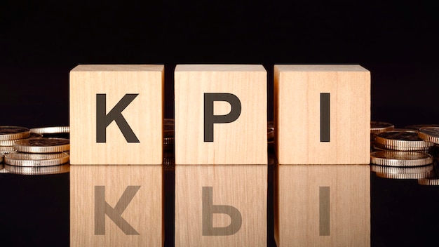 Kpi text on wood blocks on black background with coins front view business concept