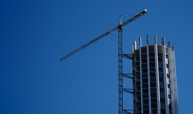 Kraan en bouwwerf tegen blauwe hemelbouw van hoogbouwconcept