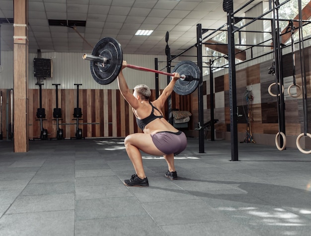 Krachtige en sterke vrouwenbodybuilder die overhead met zware barbell in moderne dwarsgymnastiek doet. Functioneel trainen. Bodybuilding en fitness