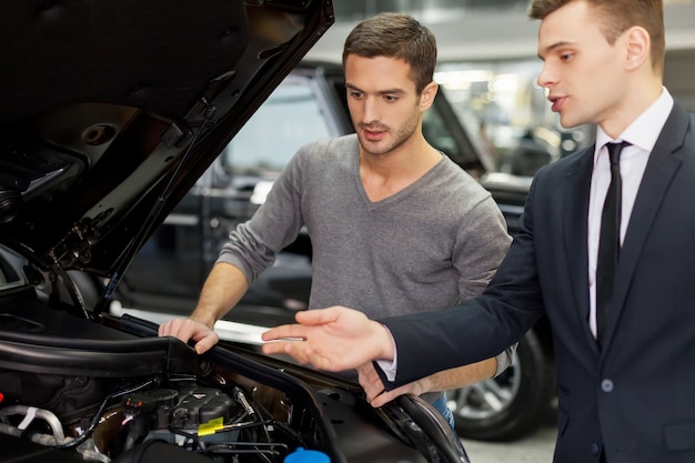 Foto krachtige motor. knappe jonge verkoper die alle autokenmerken aan de klant laat zien