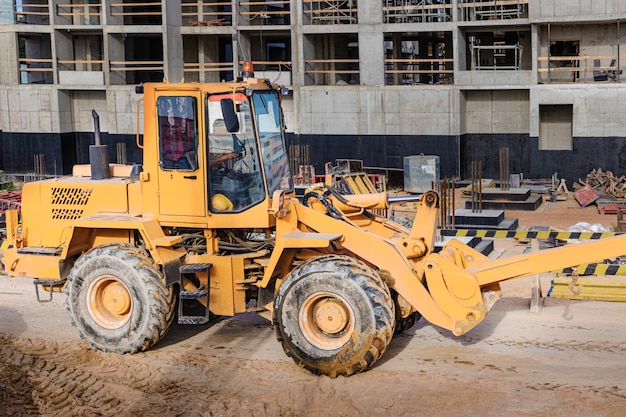 Krachtige wiellader voor het vervoeren van volumineuze goederen op de bouwplaats van een moderne woonwijk. Bouwmachines voor het hijsen en verplaatsen van lasten.