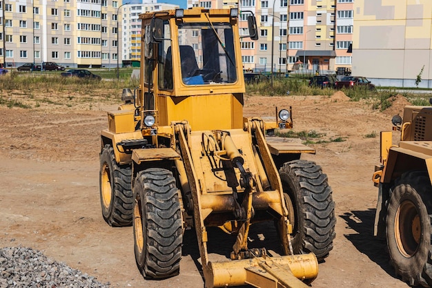 Krachtige wiellader voor het vervoeren van volumineuze goederen op de bouwplaats van een moderne woonwijk. Bouwmachines voor het hijsen en verplaatsen van lasten.