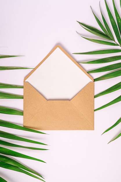 Kraft brown paper envelope with white empty card on palm leaves