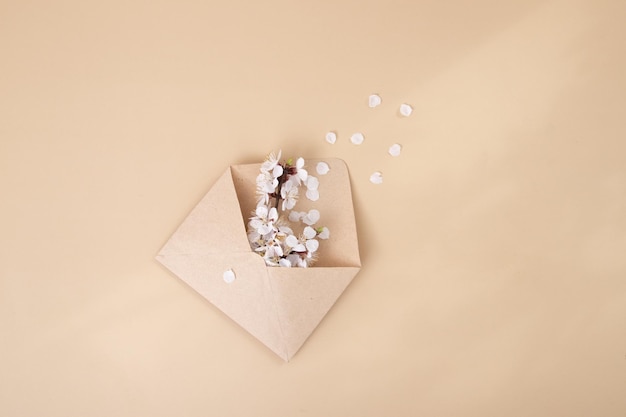 Kraft envelop met een lentetakje en witte lentebloemen op een beige ondergrond