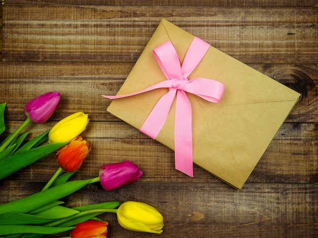 Kraft envelope tied with a pink ribbon on wooden background with tulips