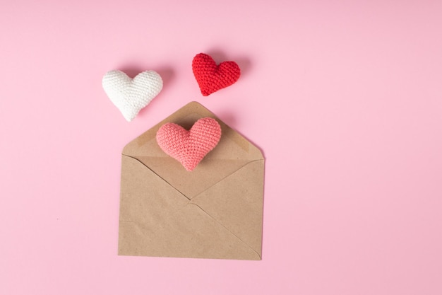 Una busta kraft con tre cuori lavorati a maglia su uno sfondo rosa banner per la cartolina di san valentino per il 14 febbraio love minimalism