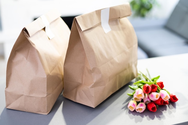 Kraft paper bags with blooming red tulips bouquet on gray
background. flowers and food delivery packaging banner copy space
mockup. donations help recycling boxes.