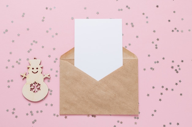 紙吹雪の星とピンクの背景に空白の白いカードのモックアップとクラフト紙封筒の手紙。