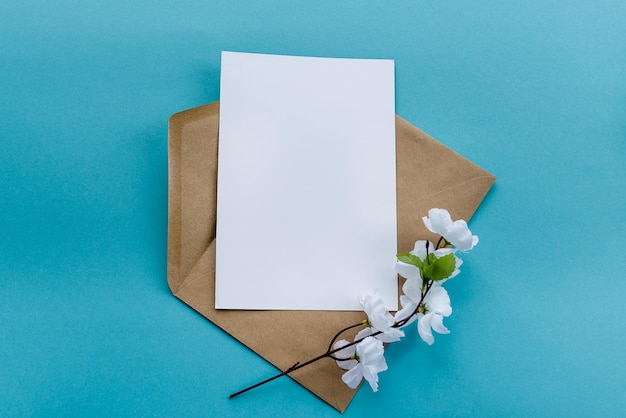 Конверт из крафт-бумаги с белыми пустыми карточками, цветами на синем фоне Подготовка открытки