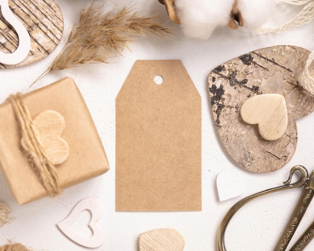 Photo kraft paper gift tag between valentines present, wooden hearts and dried flowers top view. spring scene with vertical blank label. rustic, cottage chic or bohemian mockup, copy space