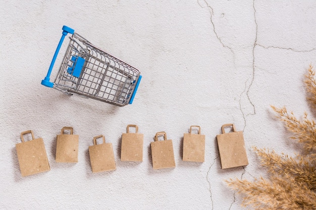 Kraft paper shopping bags in a row and a shopping cart on a\
concrete background top view