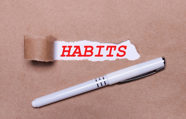 크래프트 종이에 흰색 펜과 HABITS라는 텍스트가 있는 흰색 종이 조각.