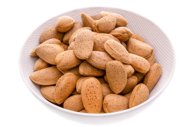 Krahmandelnunpeeled almond seeds in a white plate on a white background isolated items and products