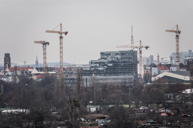 Kranen tegen gebouwen in de stad tegen een heldere lucht