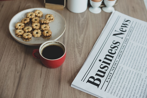 Krant, een kopje koffie en snacks op een houten tafel.