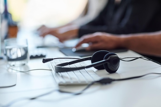 Krijg de hulp die je nodig hebt Shot van een set headsets die op een bureau liggen met werknemers op de achtergrond