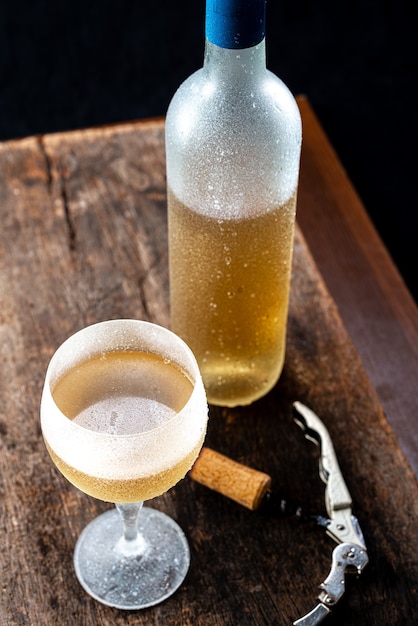 Kristalglas met witte wijn en een fles wijn die erg koud werd geserveerd op een rustieke houten tafel