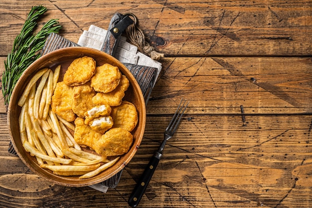 Krokant gebakken kipnuggets met frietjes in houten plaat. Houten achtergrond. Bovenaanzicht. Ruimte kopiëren.