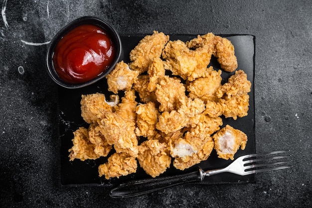 Krokant gebakken paneermeel bedekte kip popcorn met ketchup Zwarte achtergrond Bovenaanzicht