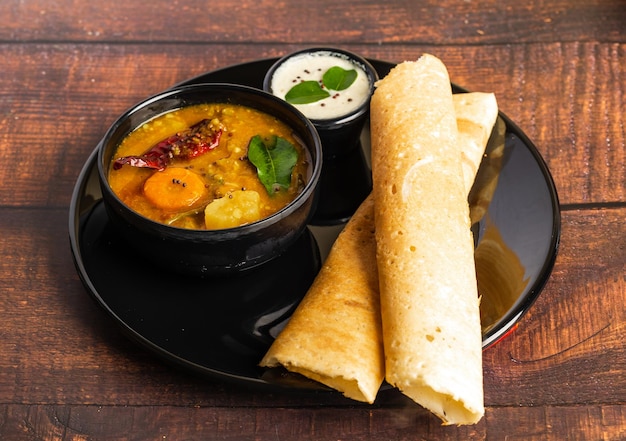 Krokante Dosa of Little Millet Dosa op een zwarte plaat. Geserveerd met sambar en chutney. Dosa.