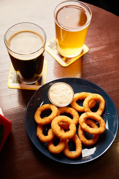 Krokante gouden uienringen bestrooid met zeezout in een kom en bierglazen op een houten tafel