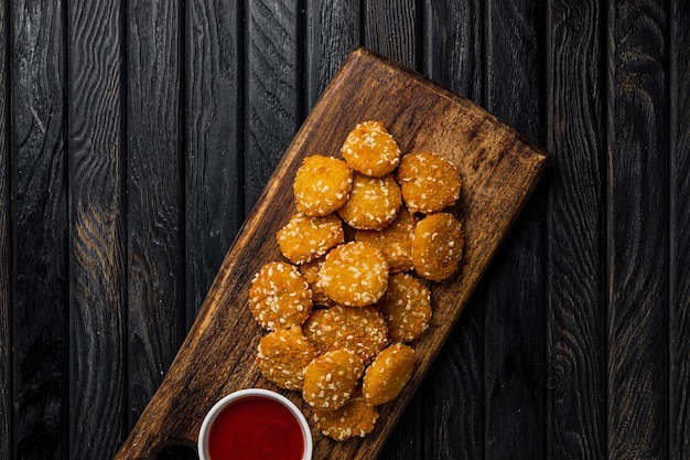 Krokante kaasnuggets met ketchup-tomatensaus geserveerd op een houten bord op een donkere houten achtergrond