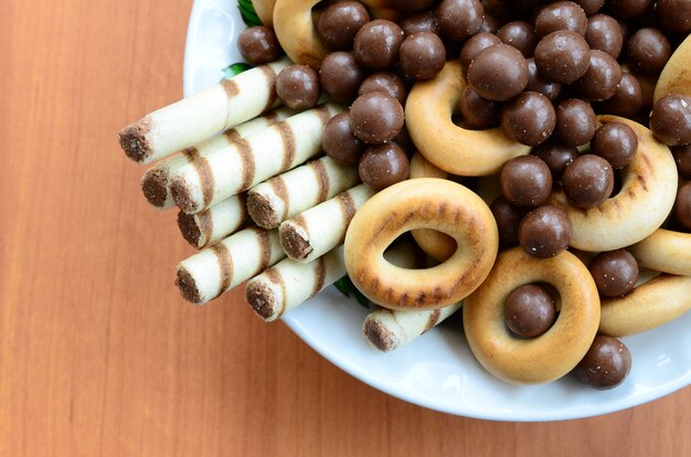 Krokante tubuli, chocolademelt ballen en bagels liggen in een witte plaat op een houten tafel. Mix van verschillende zoetigheden