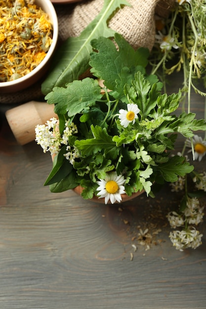 Kruiden, bessen en bloemen met mortel, op houten tafel achtergrond