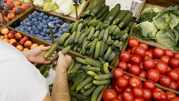 Foto kruidenier is het regelen van biologische komkommers in de winkelrekken. de verkoper vult opslagrekken op de groente- en fruitafdeling van de supermarkt