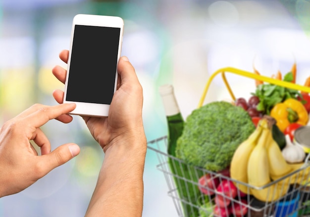 Foto kruidenier online shopping-applicatie op smartphonescherm met eten thuis op de achtergrond