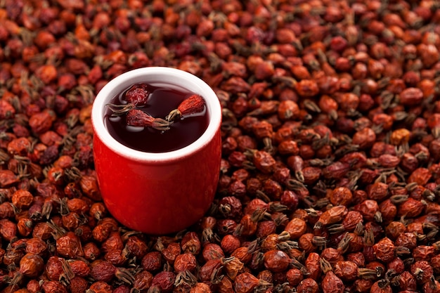 Kruidenthee gemaakt van hibiscus en gedroogde rozenbottelvruchten in keramisch glas tegen gedroogde rozenbottelvruchten