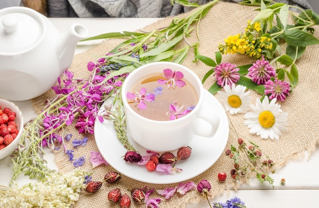 Kruidenthee met rozenbottel, kamille en klaver in een witte kop op een witte houten tafel met bloemen