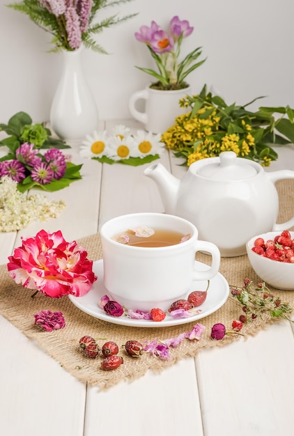 Kruidenthee met rozenbottelkamille en moerasspirea in een witte kop op een witte houten tafel met bloemen