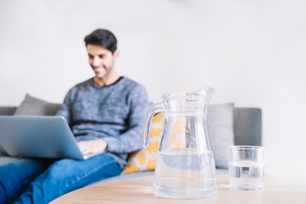 Kruik en glas dichtbij de mens met laptop