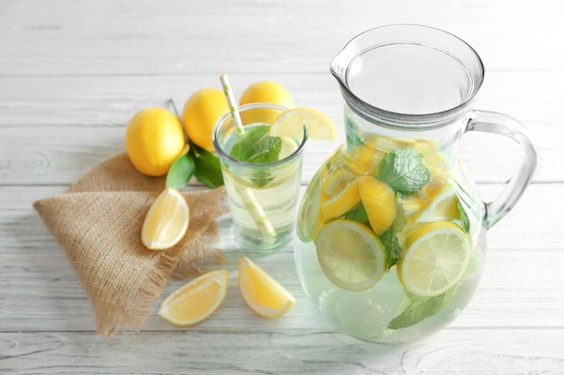 Kruik en glas met verfrissend citroenwater op houten tafel